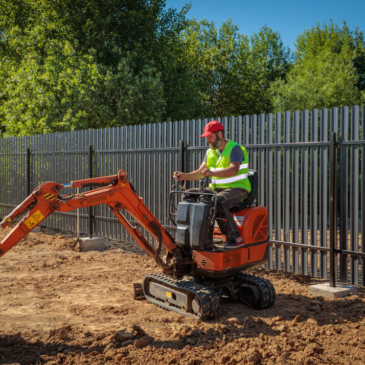 A man on a mini-excavator levels a piece of land, loosens the soil