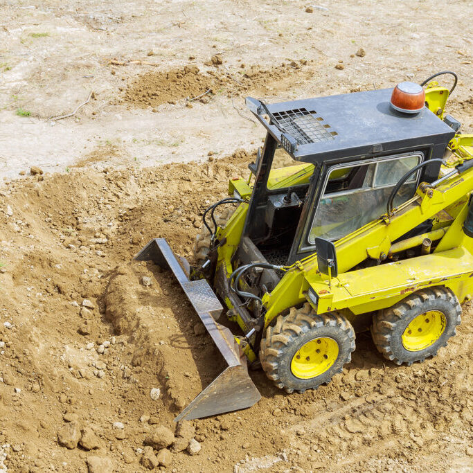 A mini tractor-loader moves and loads earth on a construction site. Leveling the surface of the land before construction.